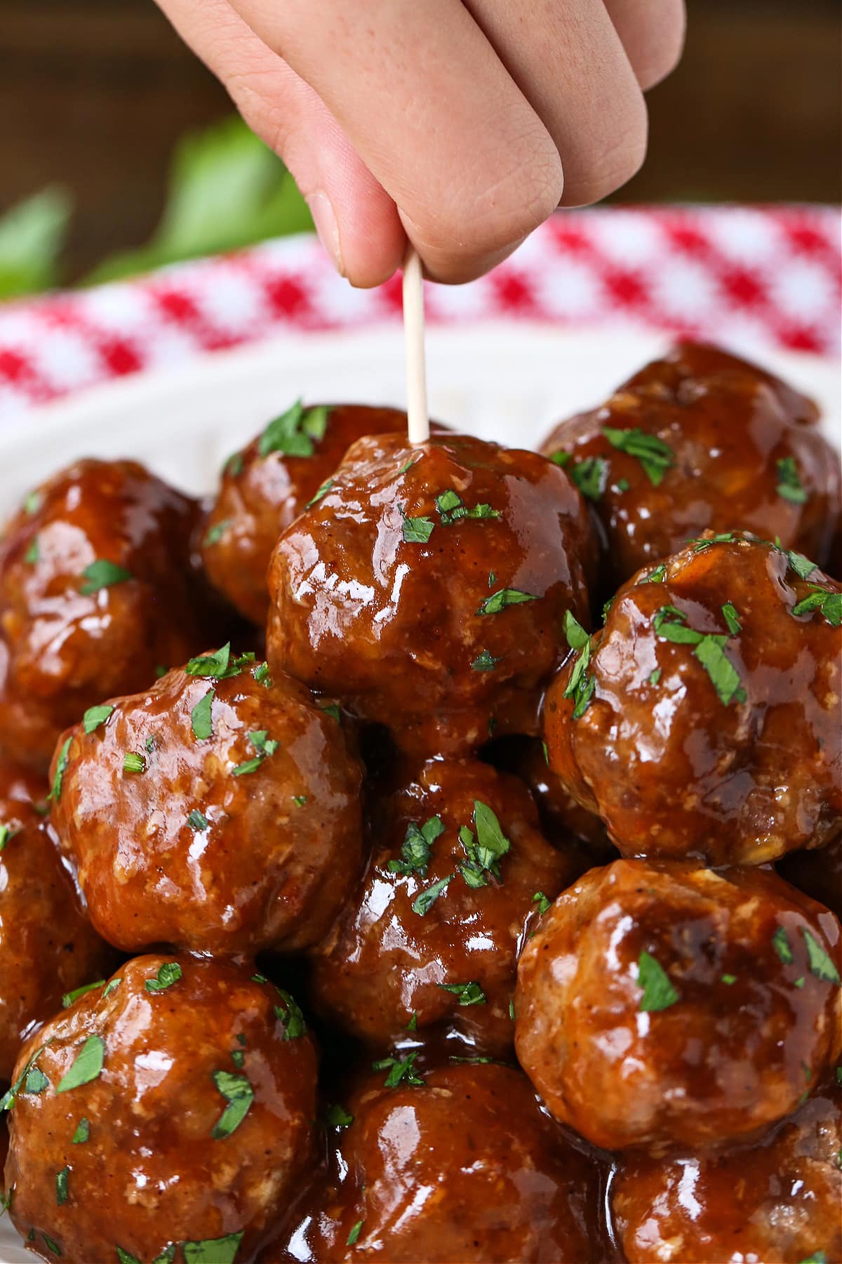 BBQ Party Meatballs are one of our favorite party appetizers! Homemade meatballs that are oven baked and tossed in a sweet and spicy sauce. hand grabbing a meatball with a toothpick