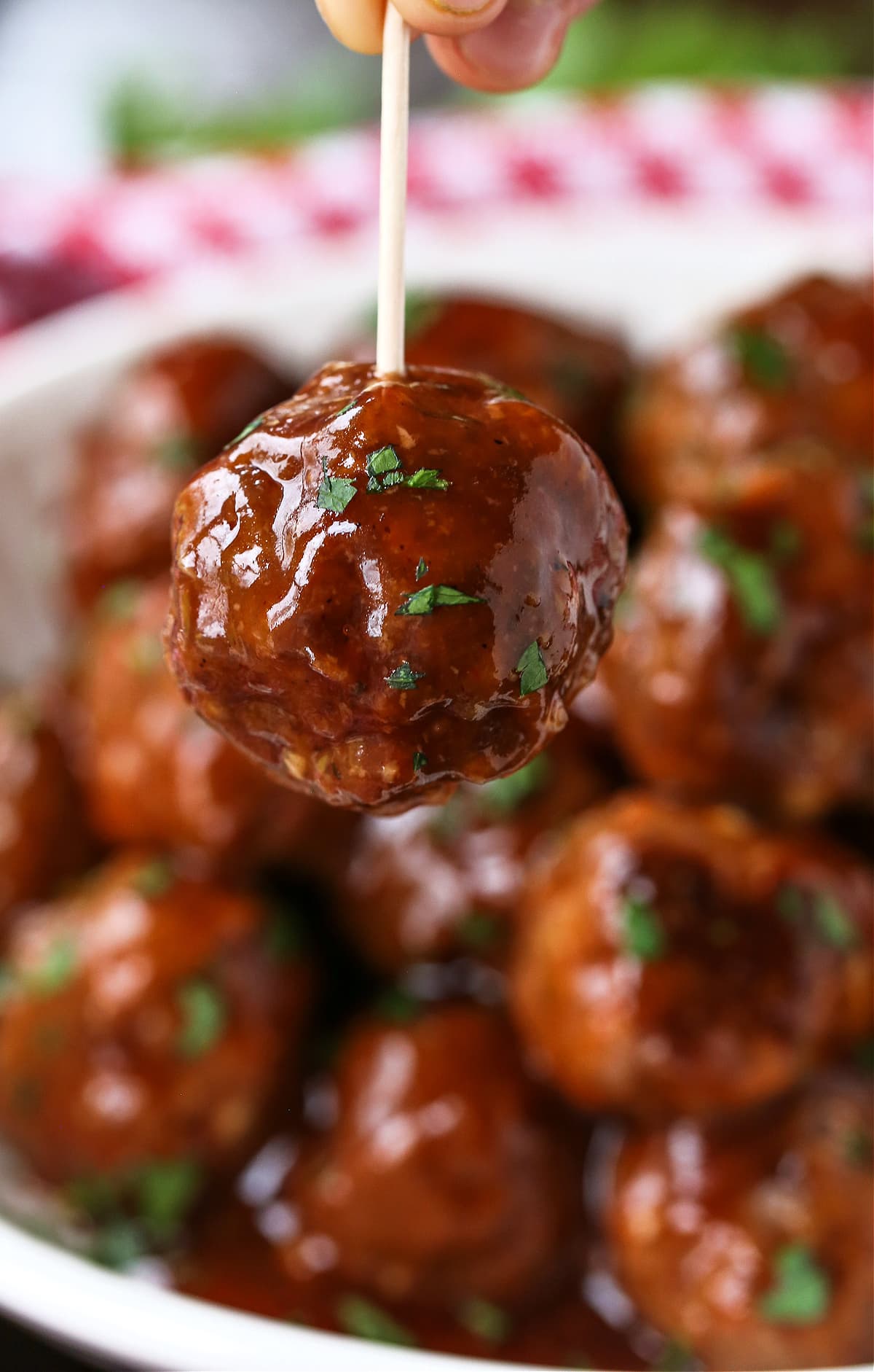 BBQ Party Meatballs are one of our favorite party appetizers! Homemade meatballs that are oven baked and tossed in a sweet and spicy sauce. meatball held up with toothpick