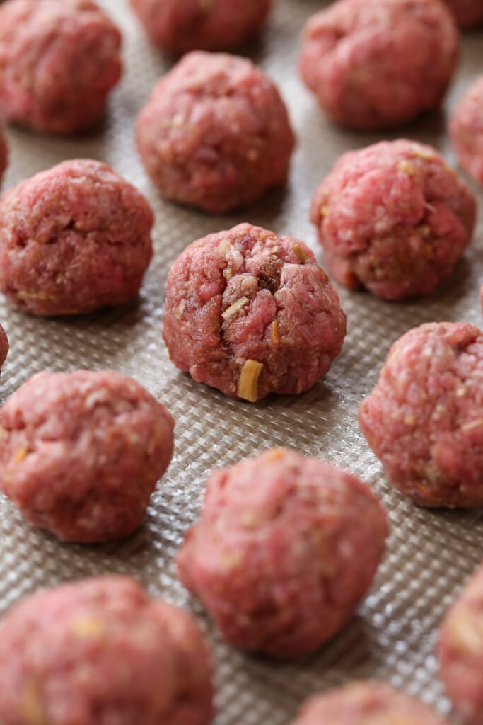 BBQ Party Meatballs are one of our favorite party appetizers! Homemade meatballs that are oven baked and tossed in a sweet and spicy sauce. raw meatballs on baking sheet