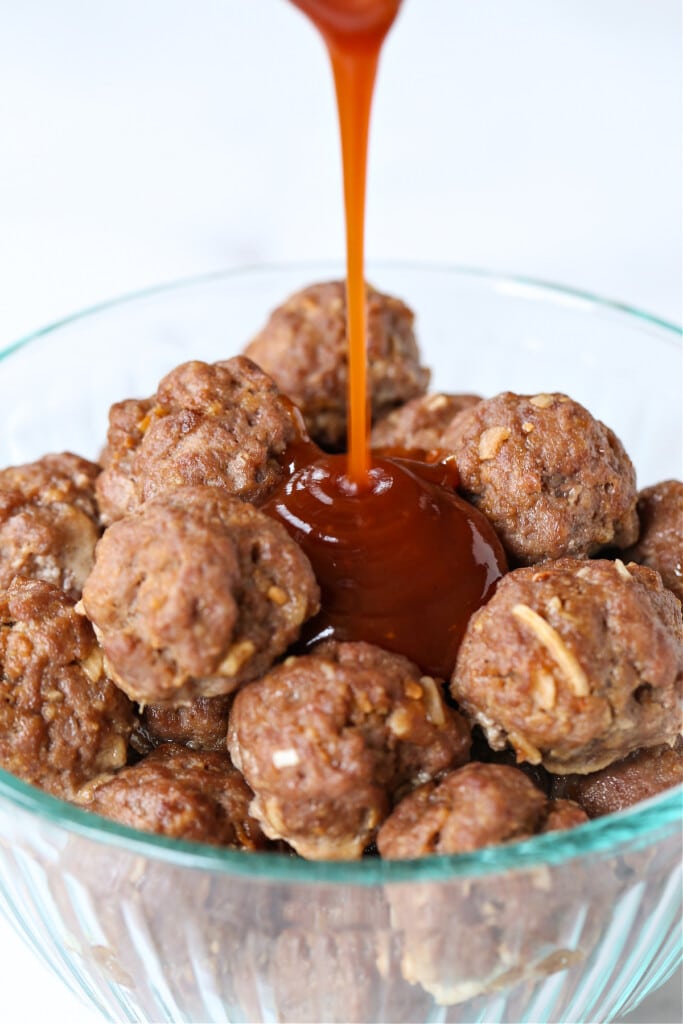 BBQ Party Meatballs are one of our favorite party appetizers! Homemade meatballs that are oven baked and tossed in a sweet and spicy sauce. meatballs in a bowl with bbq sauce pouring on top