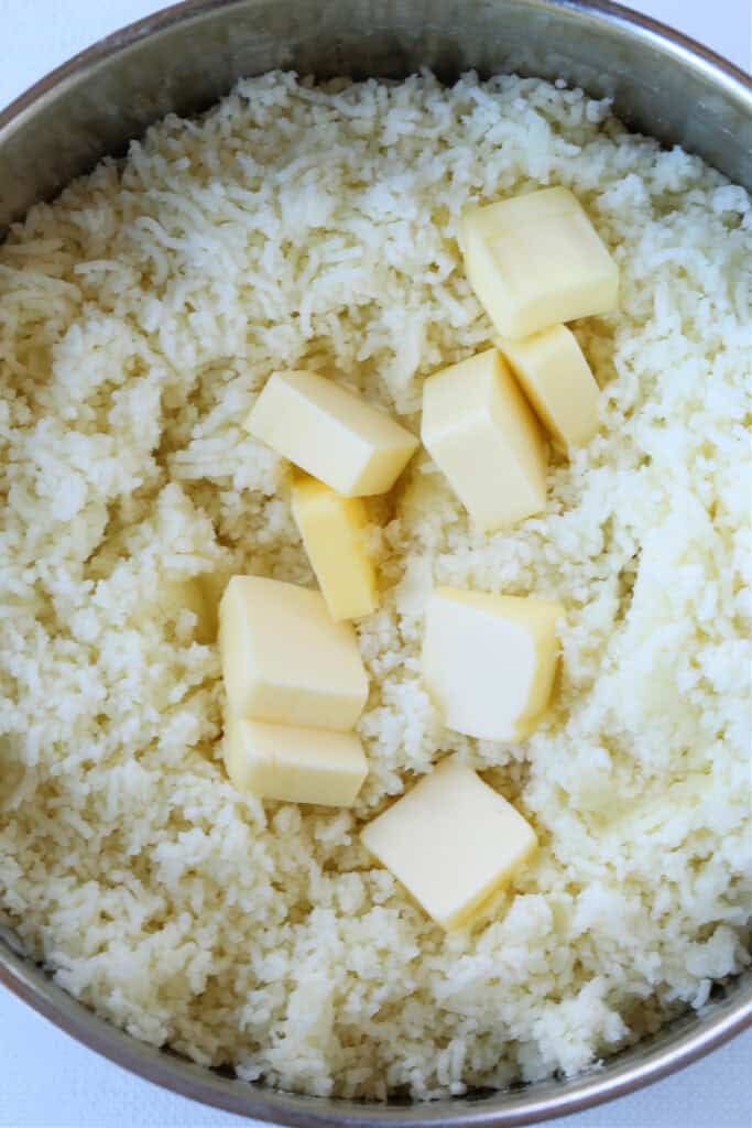 Our Fluffy Mashed Potatoes are so smooth and creamy, you won't make them any other way! A key tool makes these potatoes the best! butter in a pot of riced potatoes