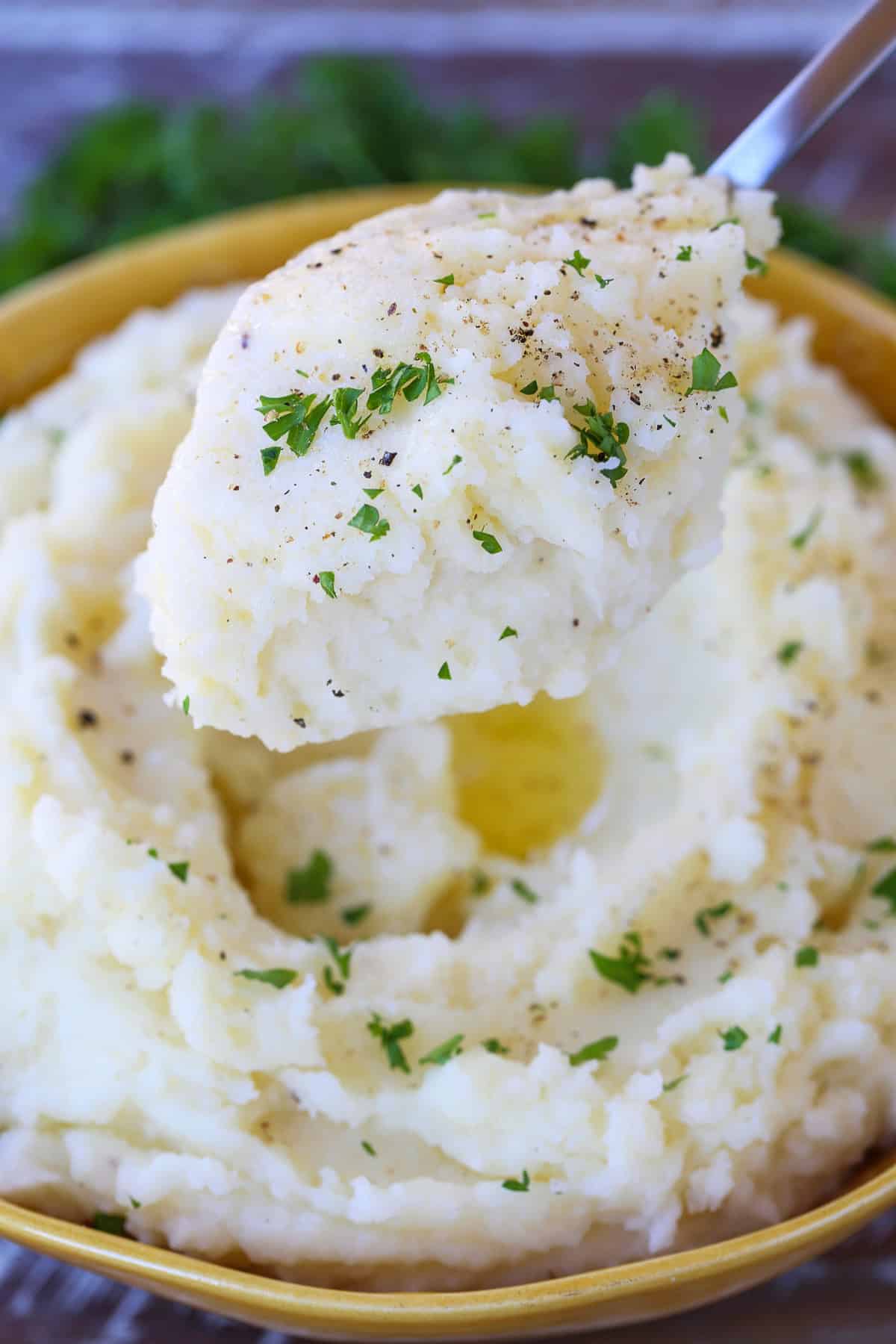 Our Fluffy Mashed Potatoes are so smooth and creamy, you won't make them any other way! A key tool makes these potatoes the best! mashed potatoes on spoon with thyme
