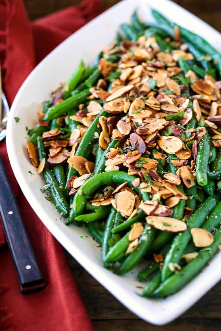 green beans with sliced almonds on a white platter with forks