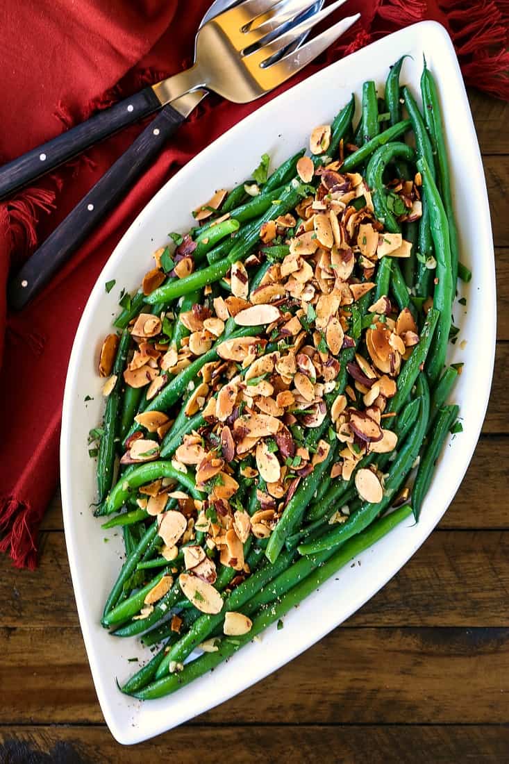 Green beans on a platter with sliced almonds and maroon napkin