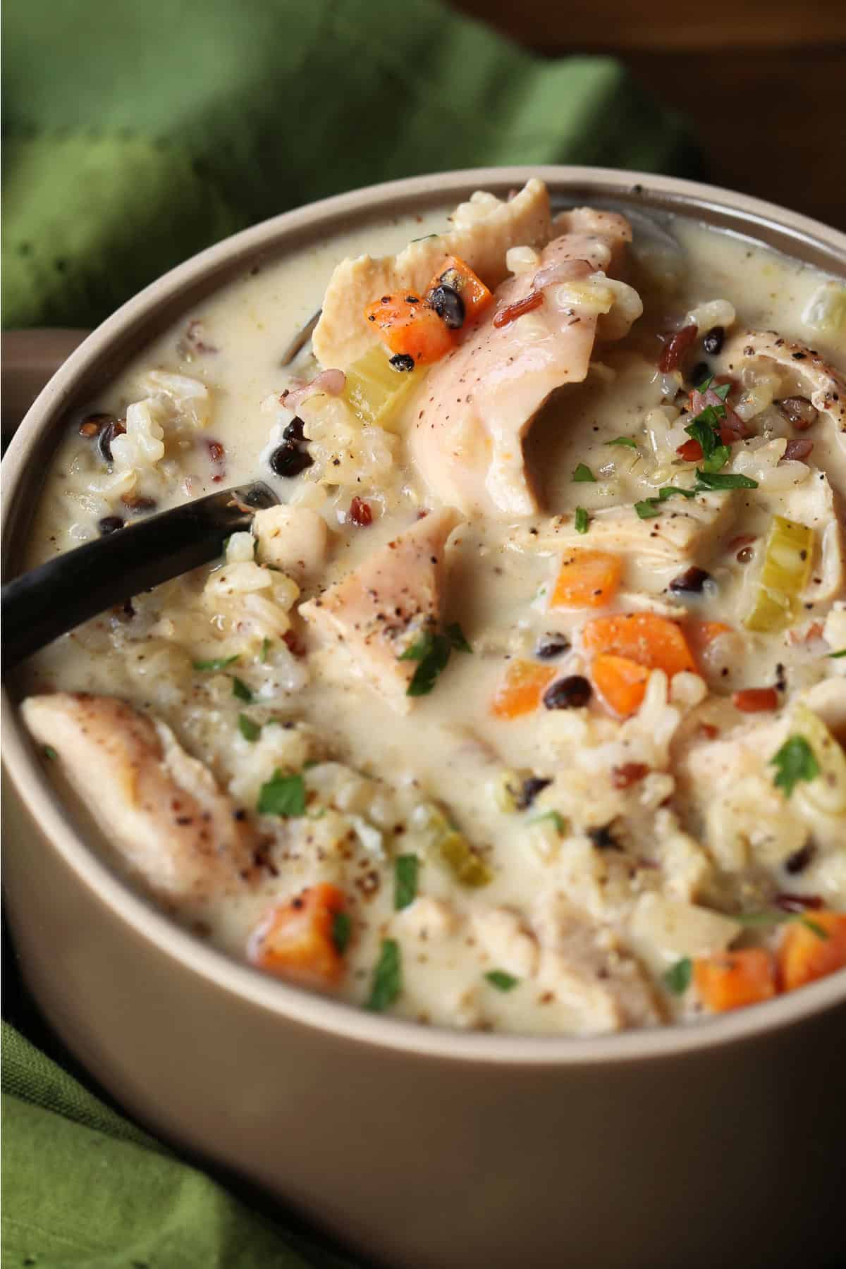 Our Turkey Wild Rice Soup is so cozy and comforting! Tender turkey with rice and vegetables in a smooth and creamy, sherry infused broth. spoon in bowl of turkey soup with rice and vegetables