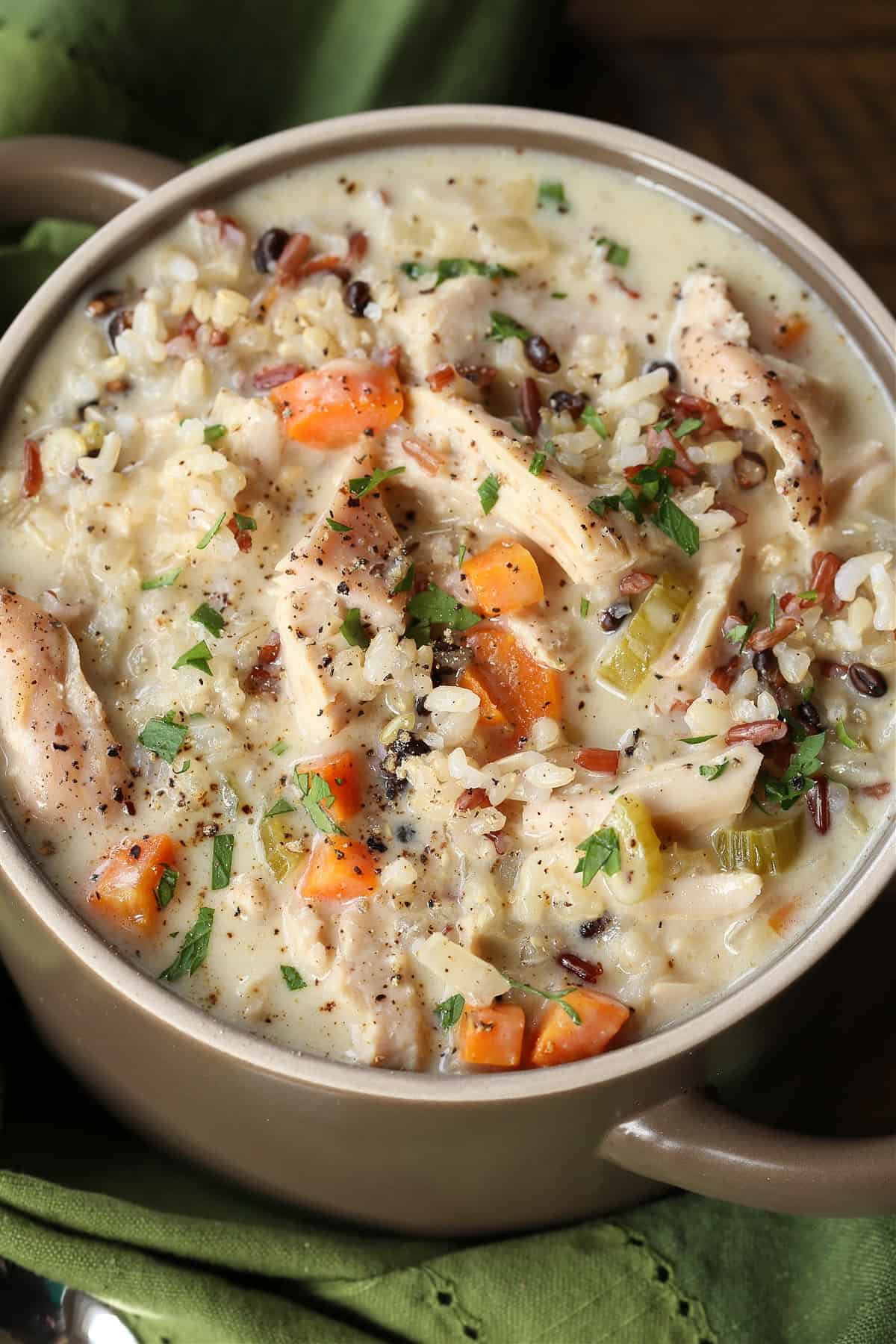 Our Turkey Wild Rice Soup is so cozy and comforting! Tender turkey with rice and vegetables in a smooth and creamy, sherry infused broth. turkey and rice soup in a crock with green napkin