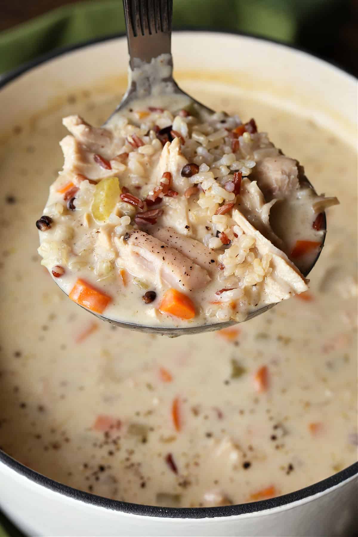 Our Turkey Wild Rice Soup is so cozy and comforting! Tender turkey with rice and vegetables in a smooth and creamy, sherry infused broth. ladle with creamy turkey soup over pot