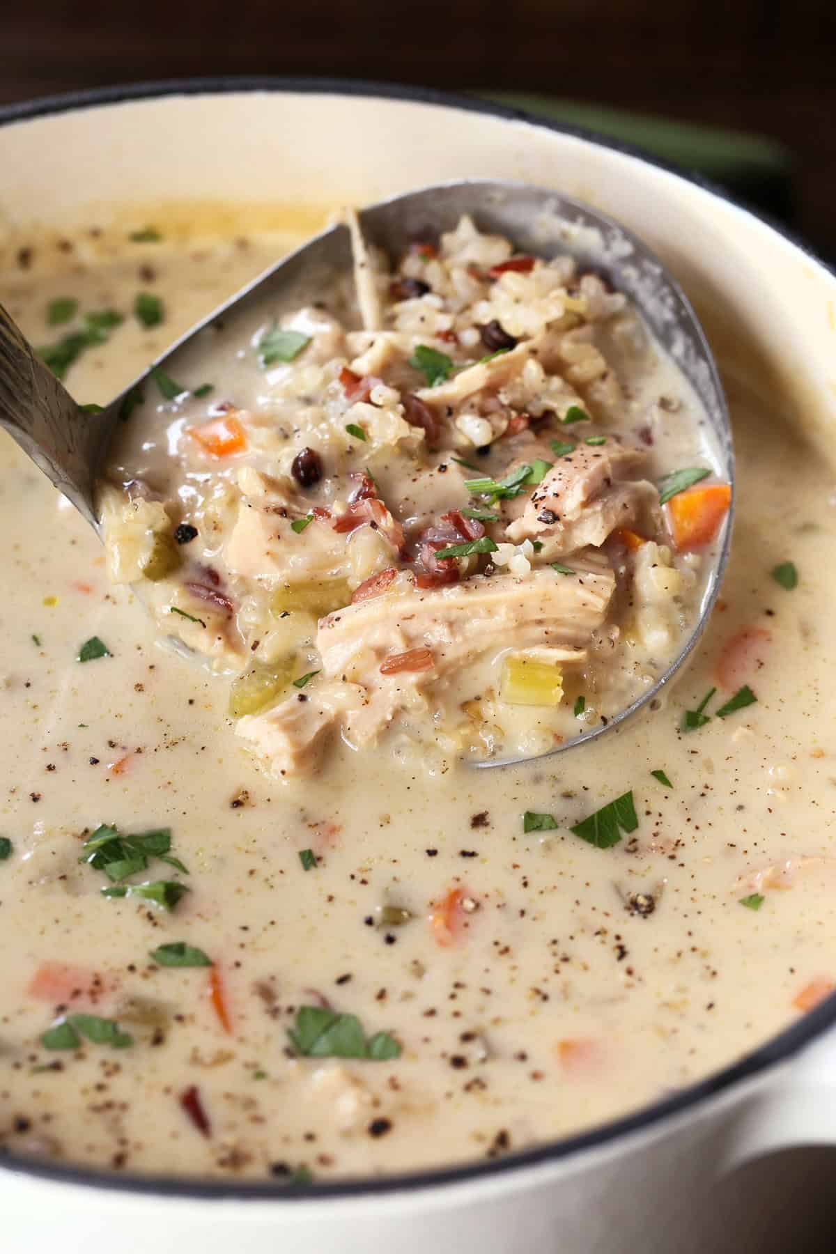 Our Turkey Wild Rice Soup is so cozy and comforting! Tender turkey with rice and vegetables in a smooth and creamy, sherry infused broth. ladle in pot of turkey soup with rice and vegetables