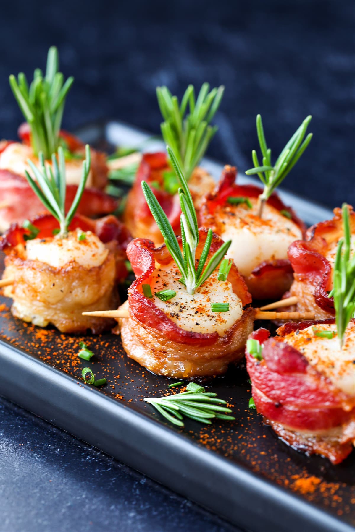Bacon Wrapped Scallops are a holiday classic appetizer! We've got a hack to make sure that the bacon is actually crispy and not rubbery! scallops wrapped in bacon on platter garnished with rosemary