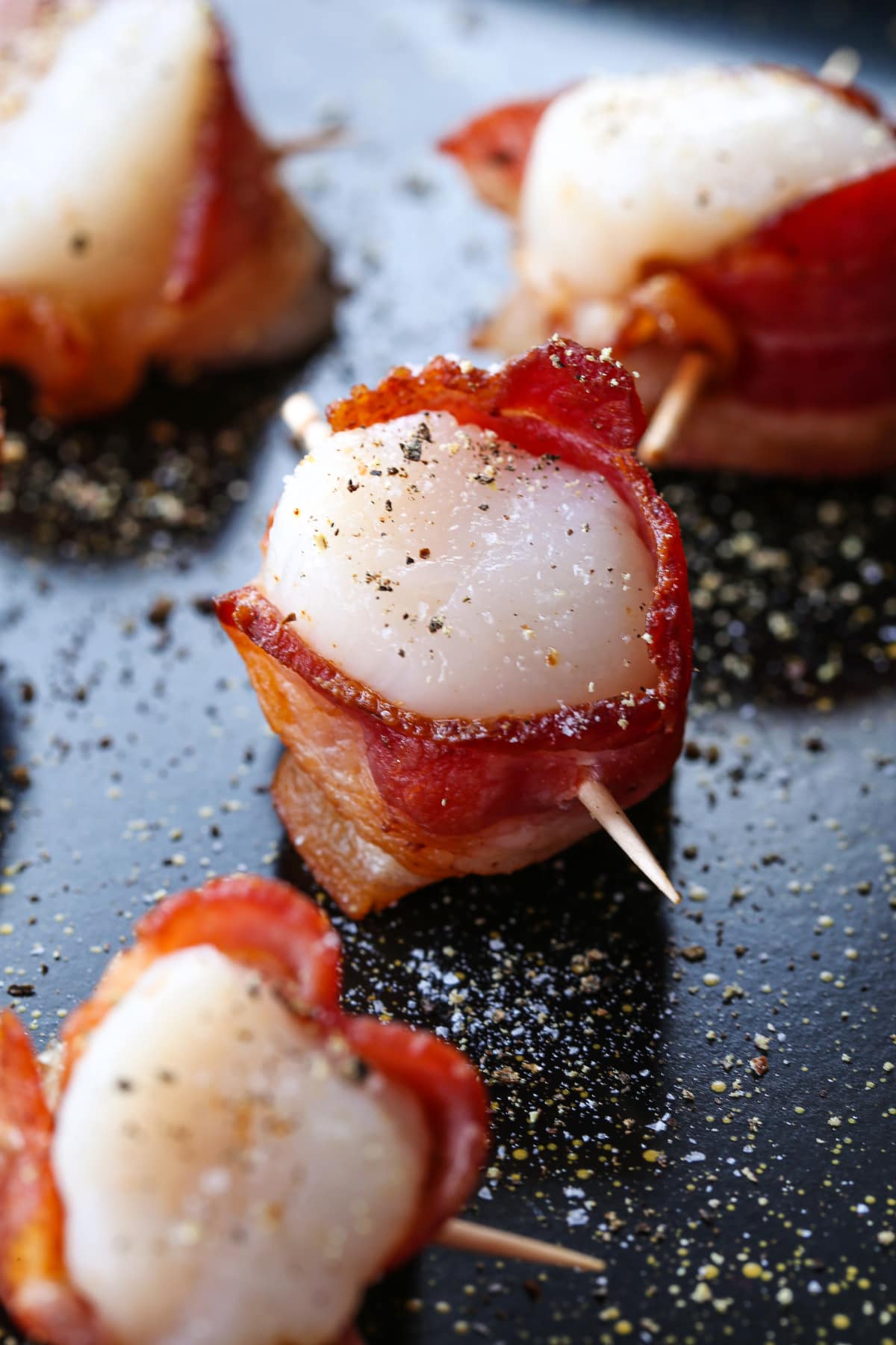 Bacon Wrapped Scallops are a holiday classic appetizer! We've got a hack to make sure that the bacon is actually crispy and not rubbery! raw scallop wrapped with bacon