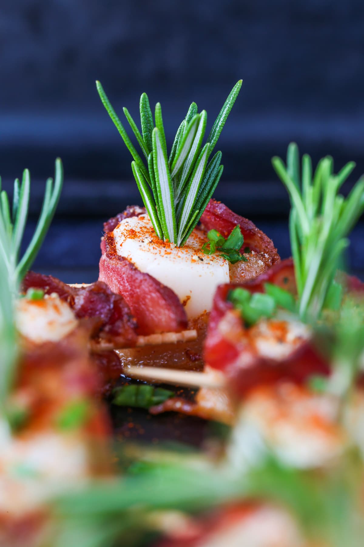 Bacon Wrapped Scallops are a holiday classic appetizer! We've got a hack to make sure that the bacon is actually crispy and not rubbery! scallops wrapped in bacon on platter with rosemary