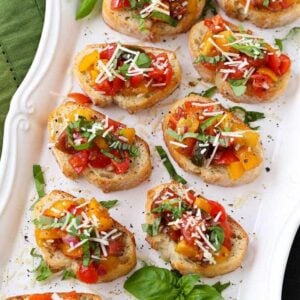 Bruschetta recipe on a white platter with parmesan cheese and basil