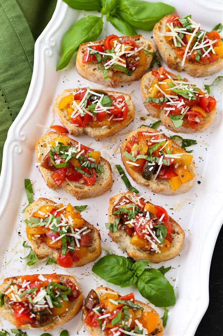 Bruschetta recipe on a white platter with parmesan cheese and basil