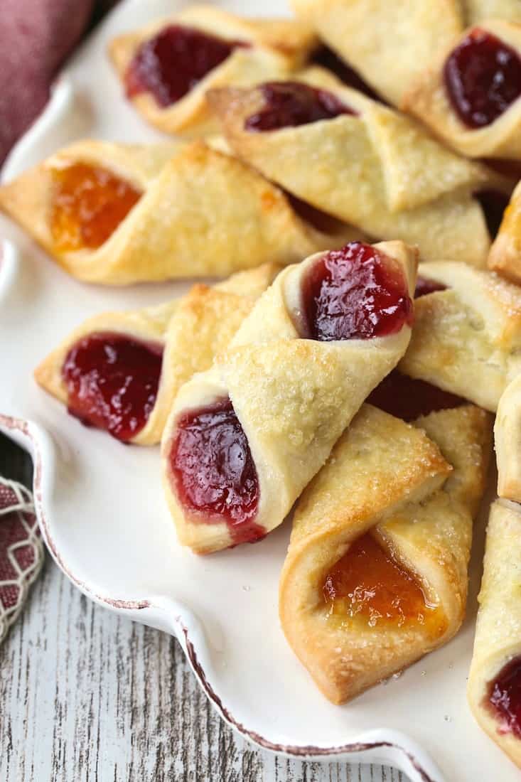 Filled with fruit jelly, Polish Cream Cheese Cookies feature buttery, slightly tangy dough wrapped around apricot and raspberry preserves. A close-up of a pile of Polish cookies filled with raspberry and apricot preserves.