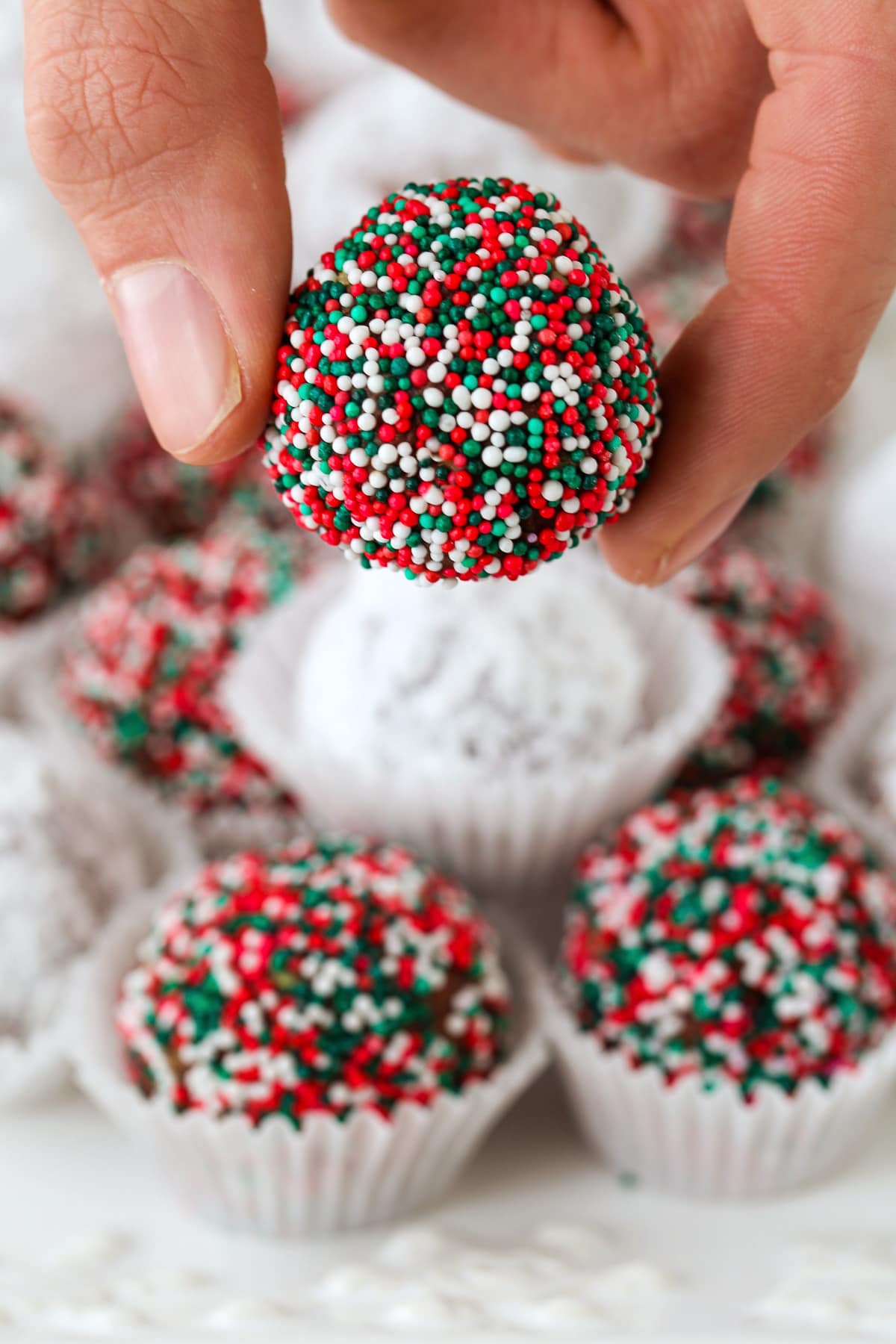 Rum Balls are a classic holiday dessert! This make ahead, festive treat can be customized for any occasion and pack a big punch of rum! fingers holding a chocolate dessert made with rum