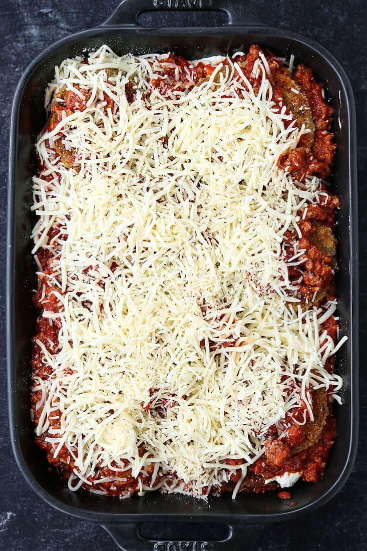 Mozzarella cheese topping an uncooked eggplant parmesan casserole.