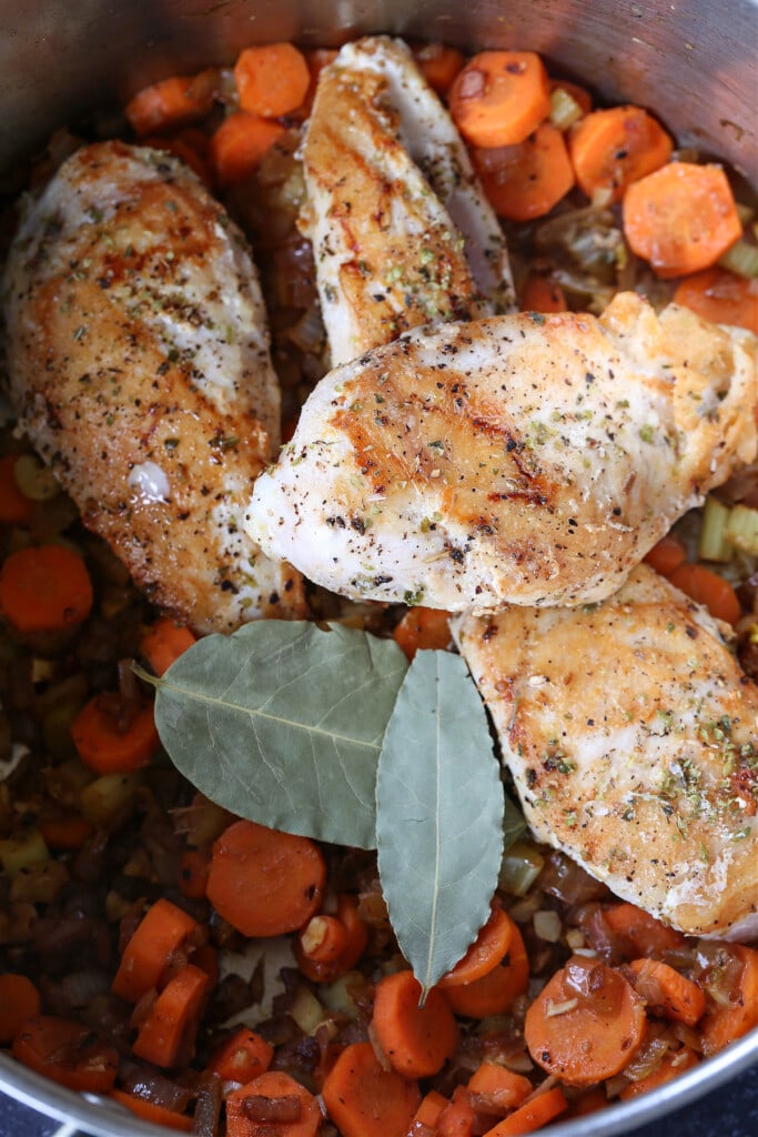 seared chicken breasts in a pot with vegetables and bay leaf