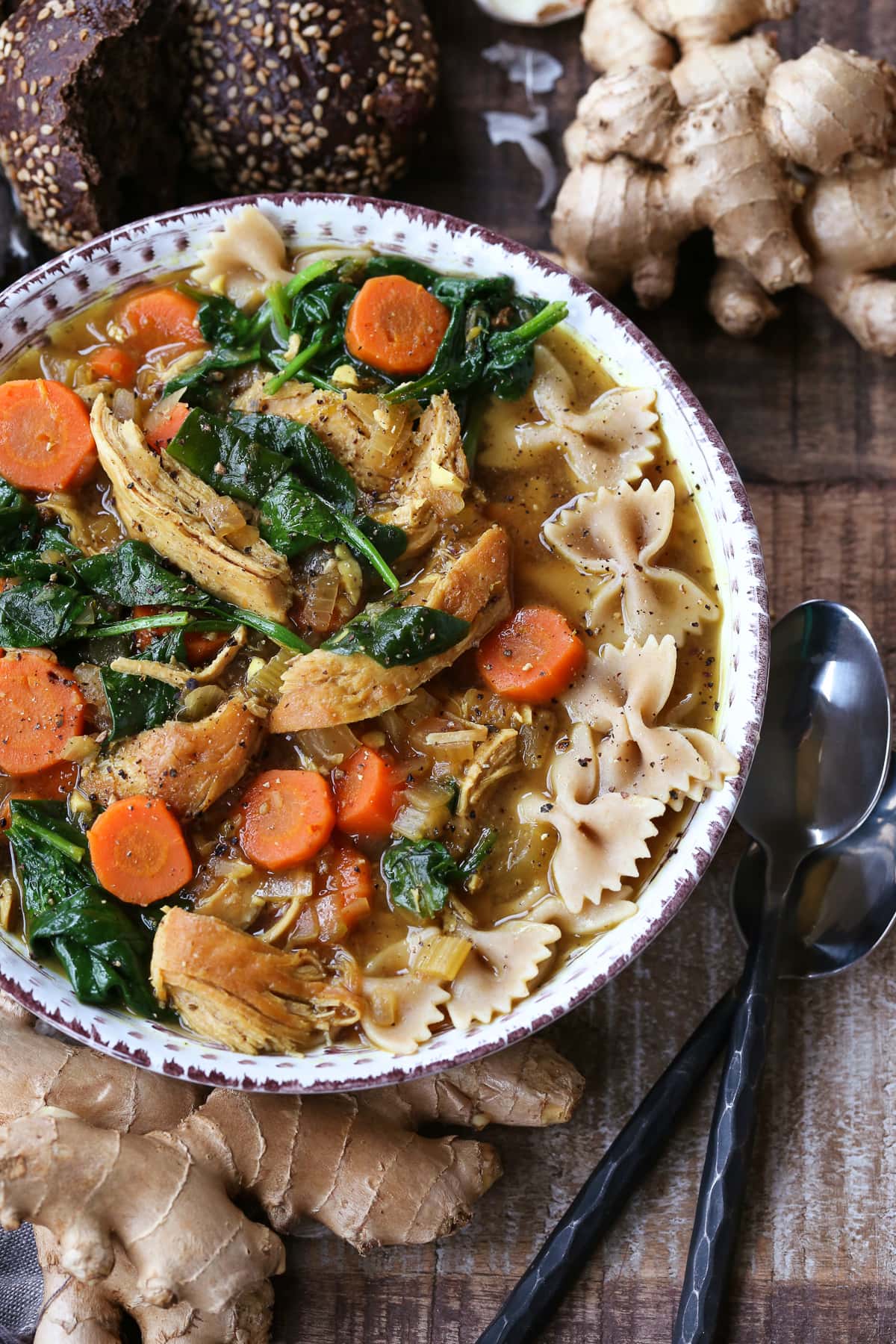 chicken soup with bow tie pasta and vegetables in a bowl with spoons on the side