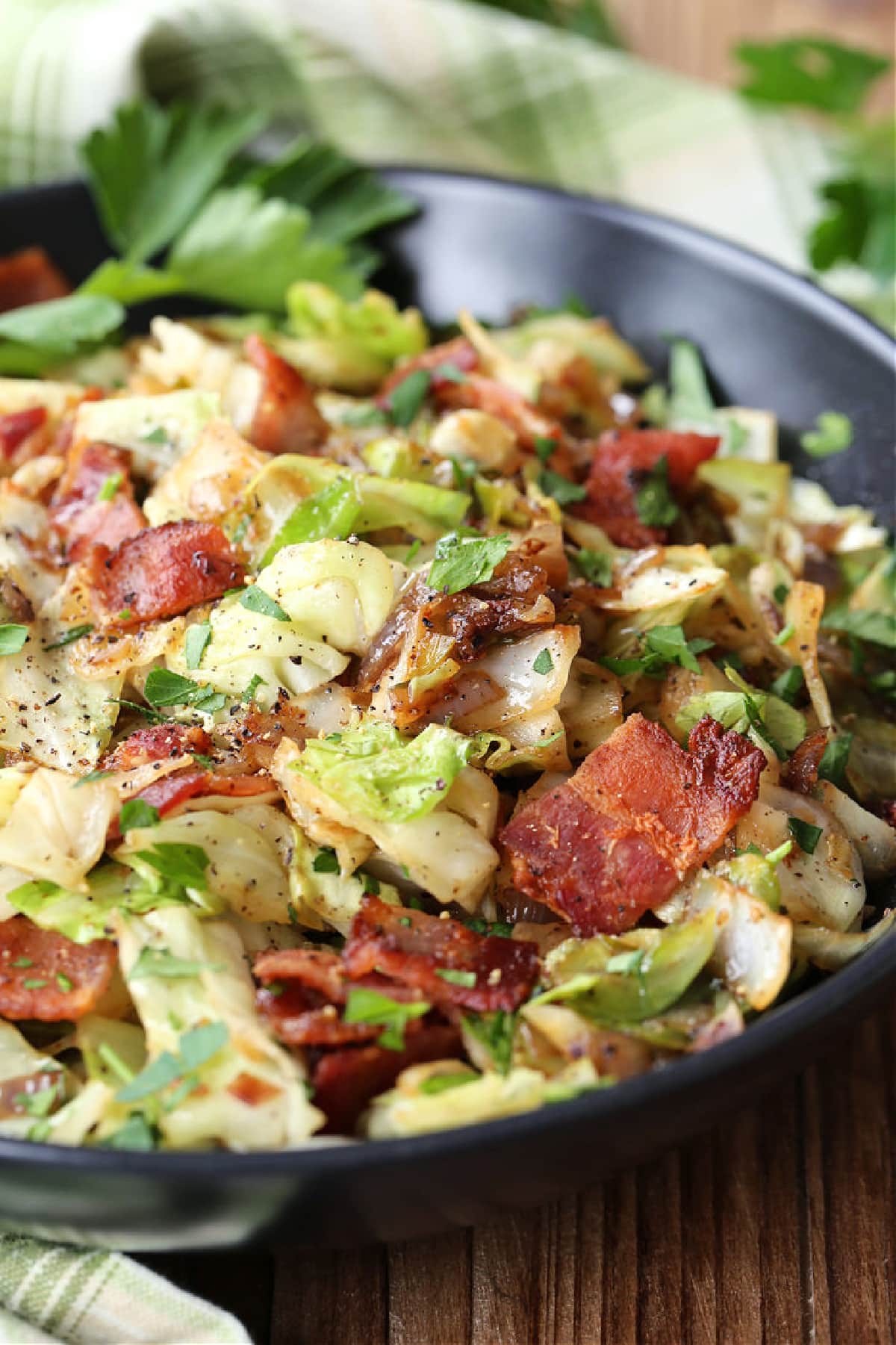 fried cabbage with bacon in black bowl with napkin