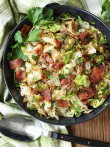 fried cabbage with bacon in a black bowl with spoon