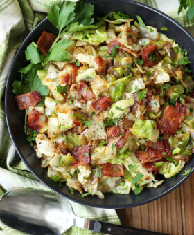 fried cabbage with bacon in a black bowl with spoon