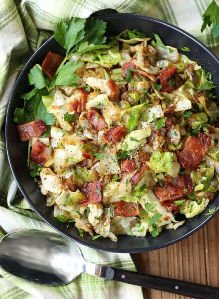 fried cabbage with bacon in a black bowl with spoon
