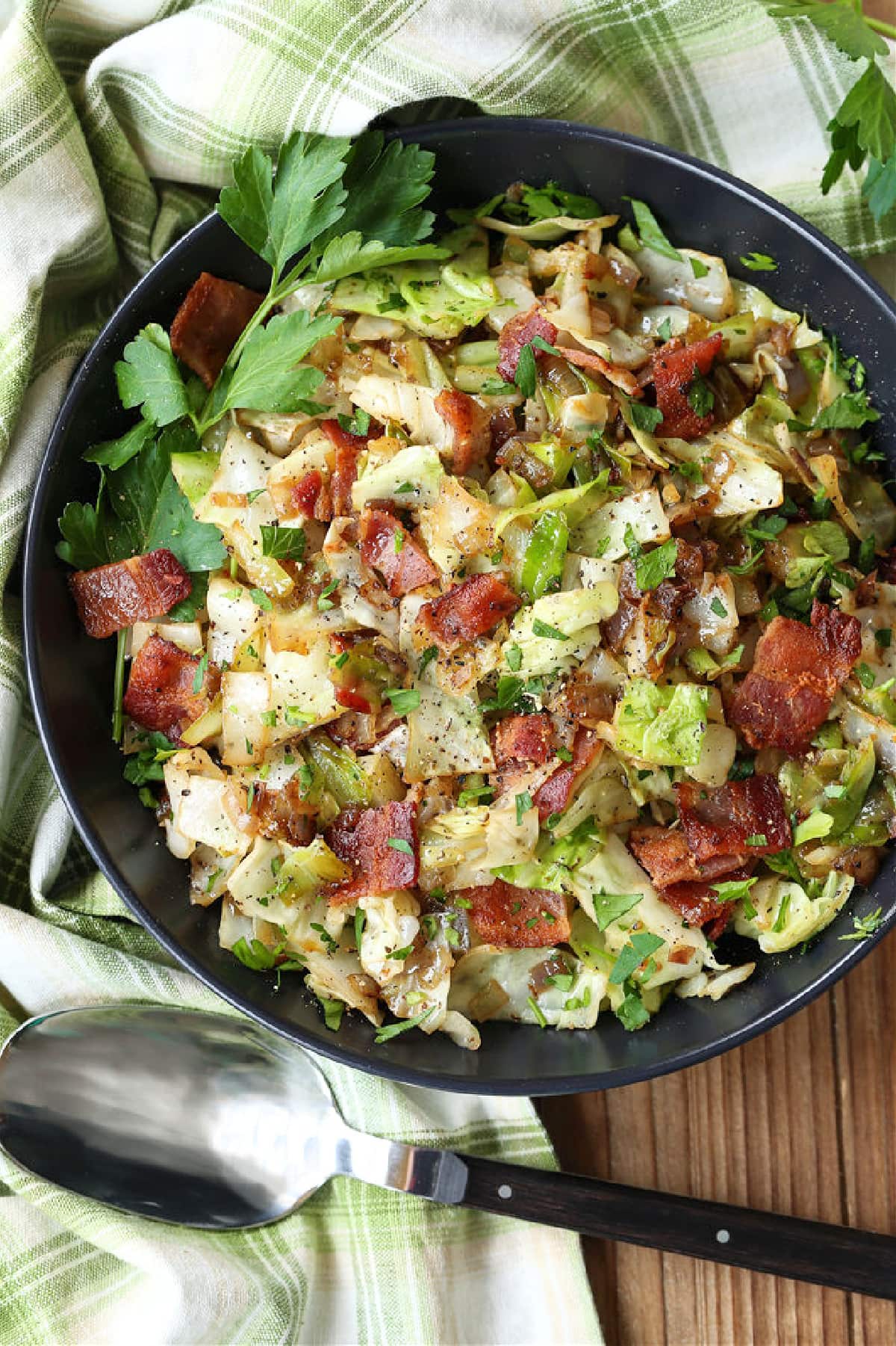 fried cabbage with bacon in a black bowl with spoon