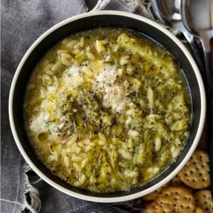 A bowlful of broccoli soup with parmesan cheese surrounded by crackers.