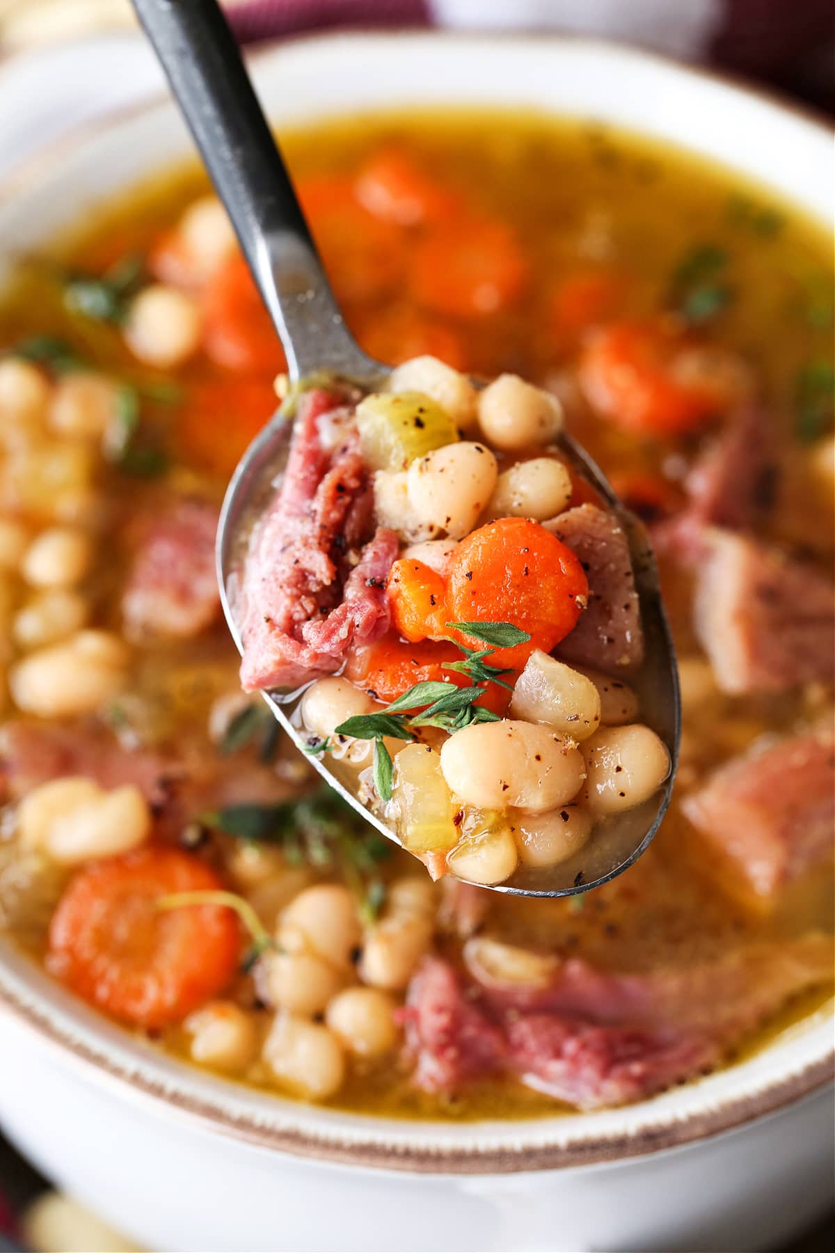Make this comforting Navy Bean Soup with your leftover ham bone! A hearty soup loaded with vegetables in a homemade ham bone broth. navy bean soup on a spoon with fresh thyme