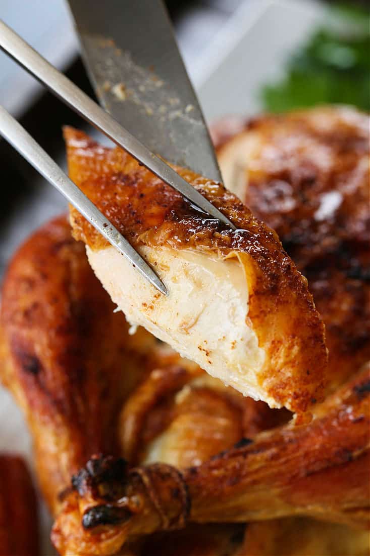 Simple Roast Chicken is perfect for Sunday dinners and for leftover meals during the week! You can even make a homemade stock with the bones! Slice of roast chicken on a serving fork