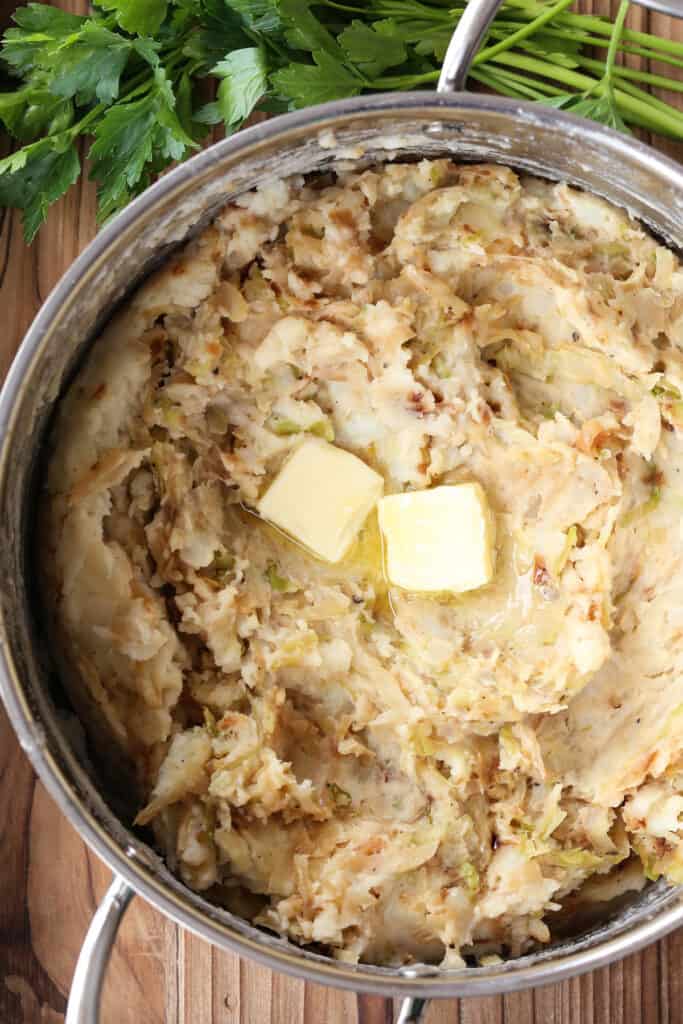 This Colcannon recipe is a St. Patrick's Day favorite! Creamy, buttery mashed potatoes blended with sweet caramelized onions and cabbage. pats of butter in a pot with mashed potatoes