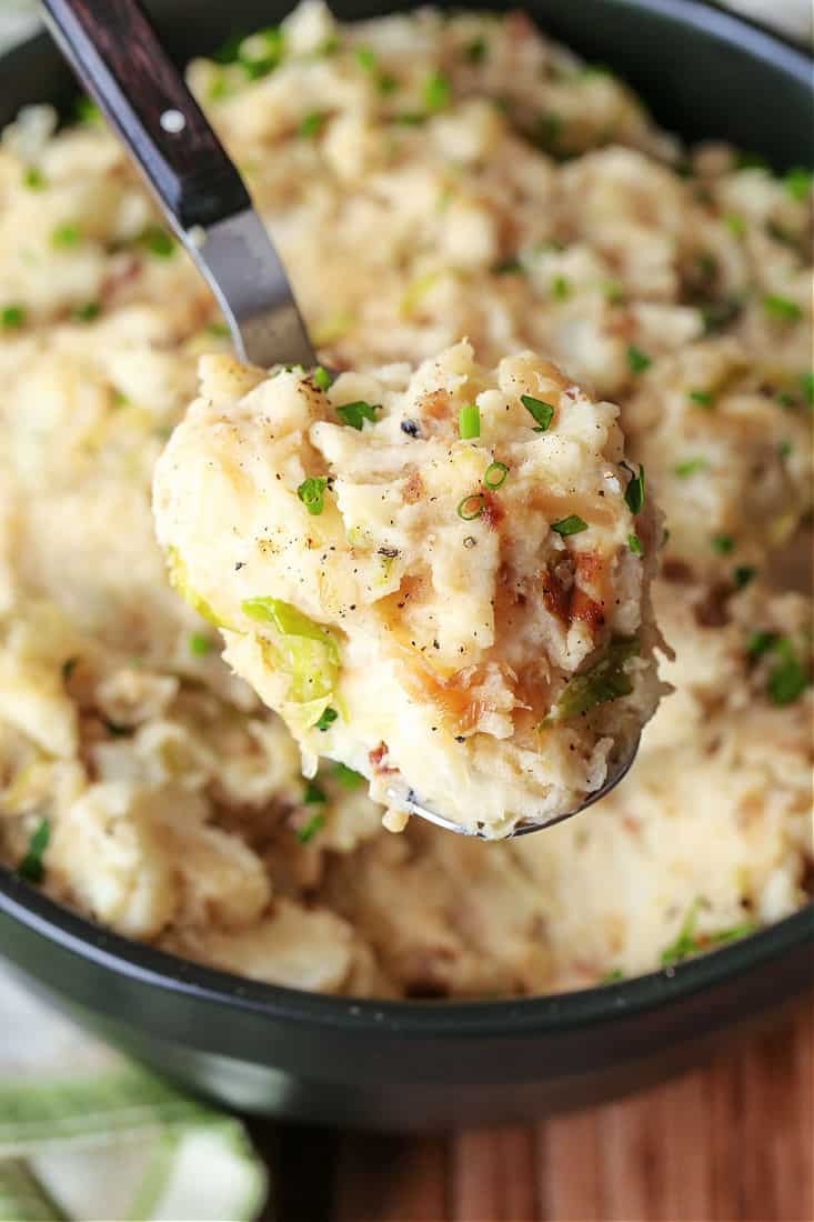 A bite of Colcannon with caramelized onion and cabbage being held up to the camera on a spoon.