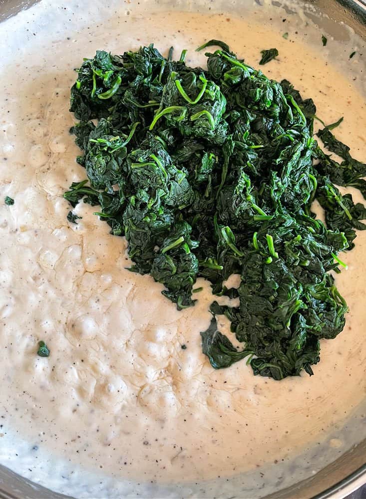 Spinach added to cream sauce in a skillet for side dish recipe