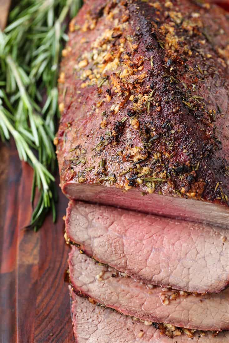 Roast beef sliced on a board with rosemary on the side