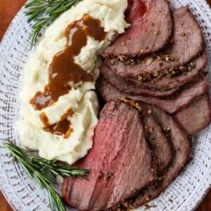 Garlic Herb Roast Beef sliced on a platter with mashed potatoes