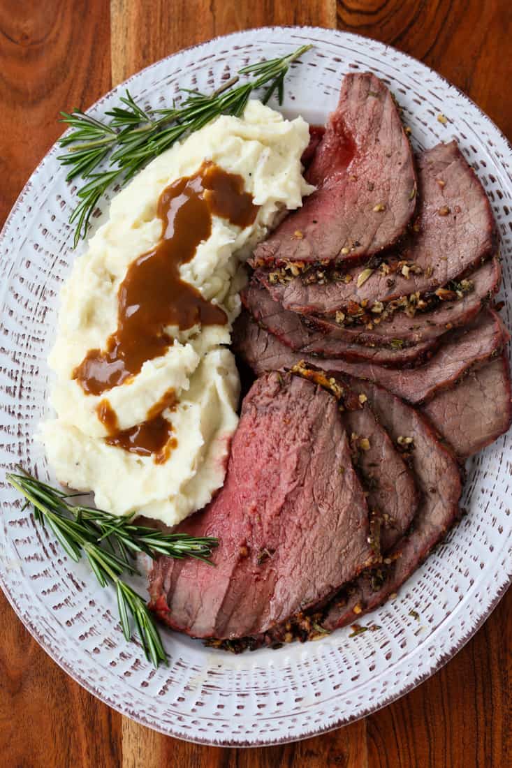 Garlic and Herb Roast Beef sliced on a platter with mashed potatoes