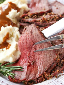 slice of rare roast beef held up with serving fork and knife