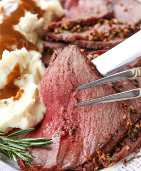 slice of rare roast beef held up with serving fork and knife