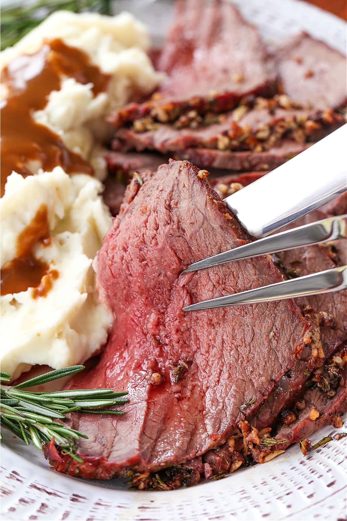 slice of rare roast beef held up with serving fork and knife