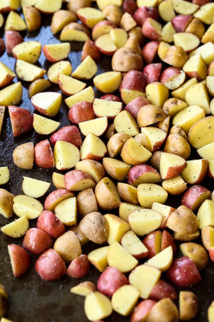 Garlic Parmesan Potatoes are a mega addicting potato side dish! Crispy, roasted potatoes tossed in our famous garlic parmesan sauce! Diced potatoes on a baking sheet for roasted potato recipe