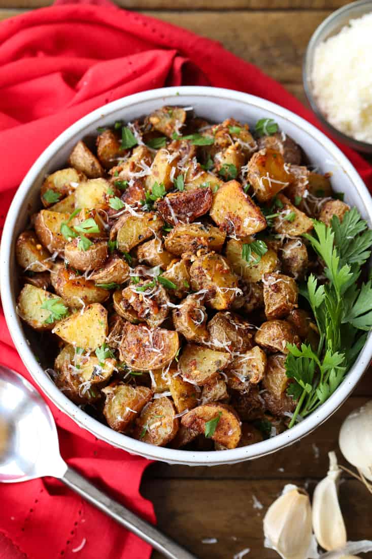 Garlic Parmesan Potatoes are a mega addicting potato side dish! Crispy, roasted potatoes tossed in our famous garlic parmesan sauce! Garlic Parmesan Potatoes in a bowl with a napkin and spoon