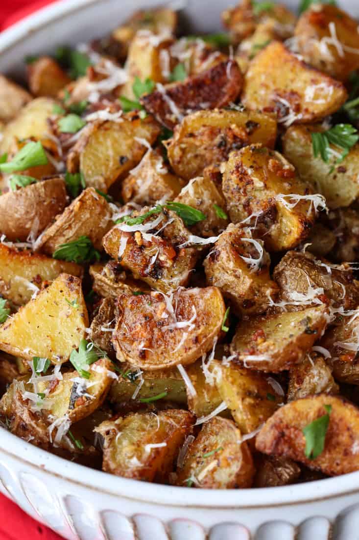 Garlic Parmesan Potatoes are a mega addicting potato side dish! Crispy, roasted potatoes tossed in our famous garlic parmesan sauce! Garlic parmesan roasted potatoes in a bowl with parmesan cheese