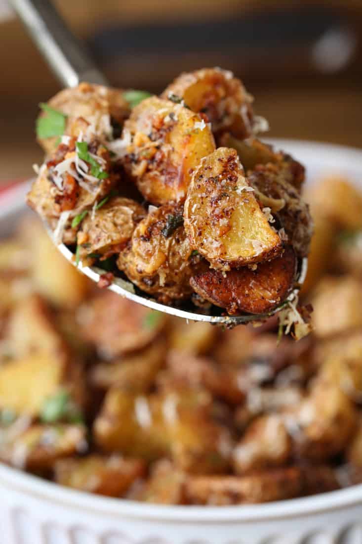 Garlic Parmesan Potatoes are a mega addicting potato side dish! Crispy, roasted potatoes tossed in our famous garlic parmesan sauce! Garlic Parmesan potatoes on a spoon