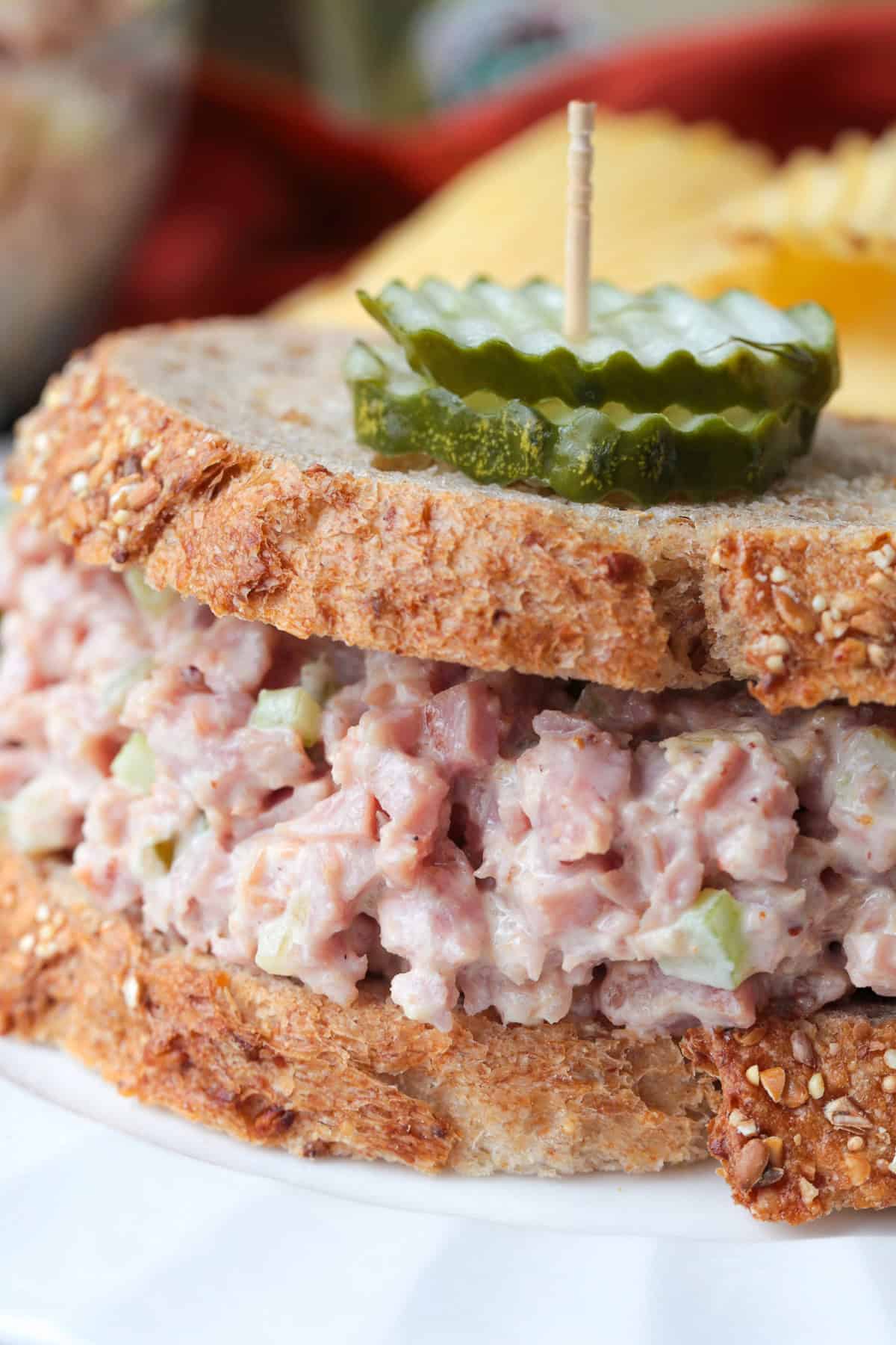 Our Ham salad recipe is the perfect way to use up leftover ham! Creamy and tangy, it’s great for sandwiches, wraps, or served with crackers. sandwich with pickles on top with a toothpick
