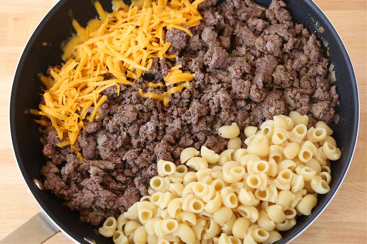 Get ready to dive into this creamy, beefy, cheesy Cheeseburger Pasta! The ultimate comfort food dinner that's ready in under 30 minutes! pasta, cooked ground beef and shredded cheese in a skillet