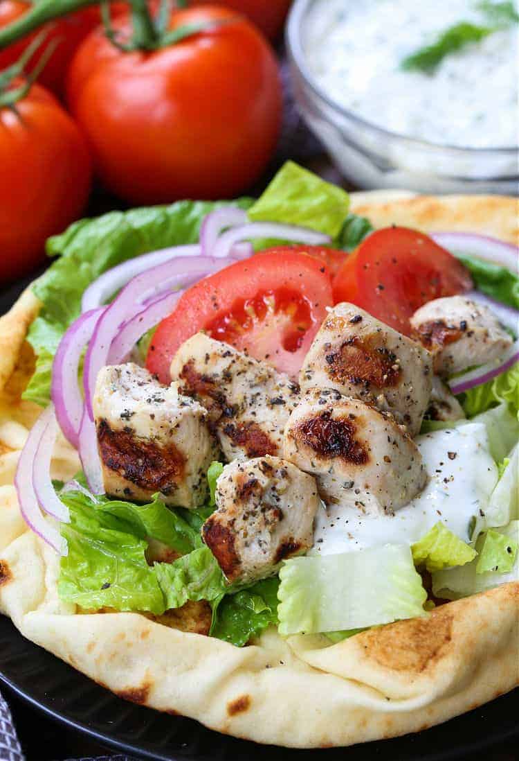 Chicken Souvlaki is a fun and easy dinner for everyday meals or parties! Grilled, marinated chicken served on pita bread with tzatziki sauce! chicken souvlaki on pita bread with tomatoes, onions and tzatzikki sauce