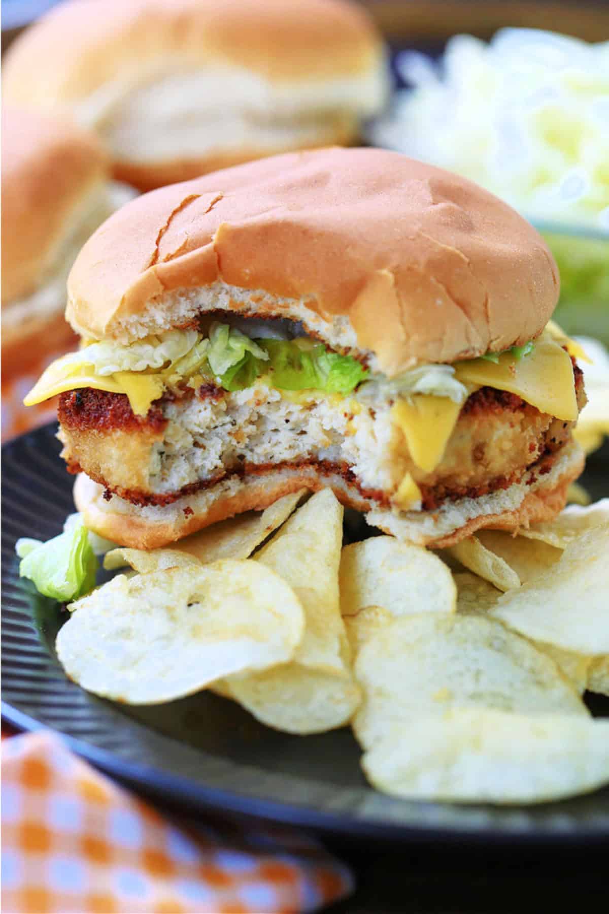 bite taken out of a chicken sandwich on a plate with chips