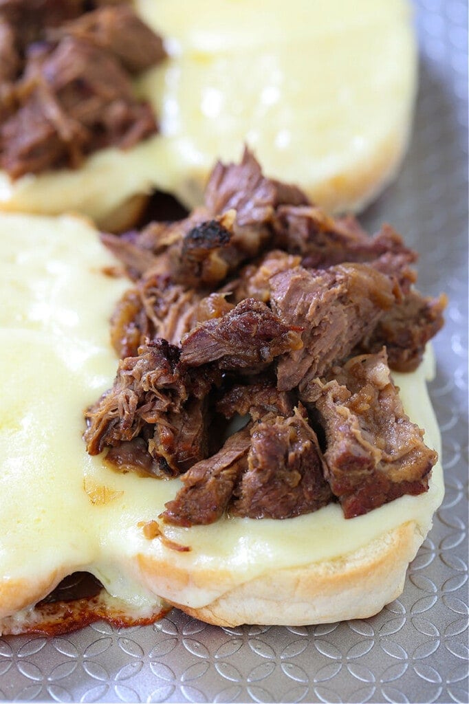 Make these Slow Cooker French Dip Sandwiches for parties or easy dinner nights! Tender, shredded beef with an au jus gravy for dipping! shredded beef on sub rolls with cheese