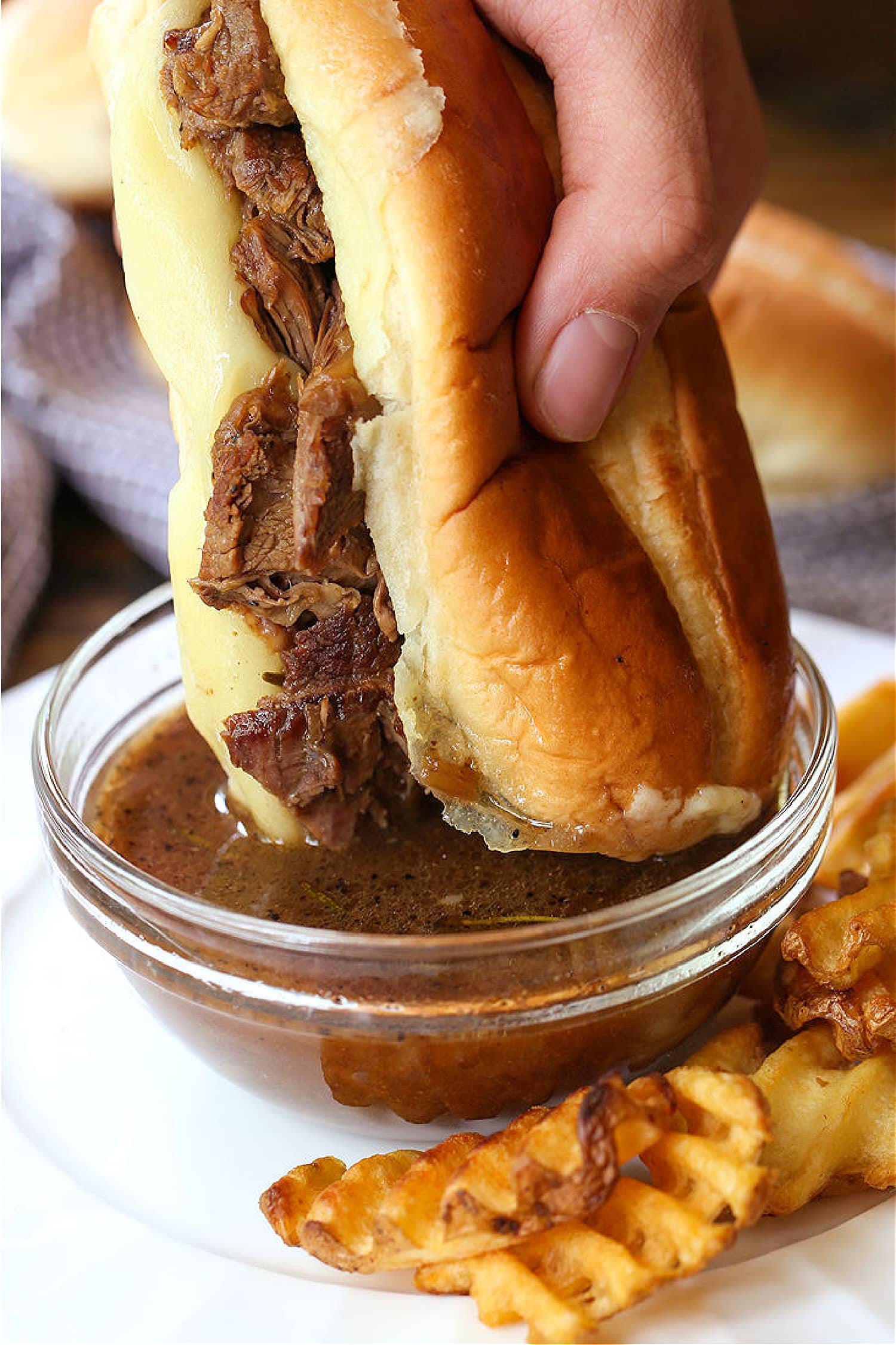 Make these Slow Cooker French Dip Sandwiches for parties or easy dinner nights! Tender, shredded beef with an au jus gravy for dipping! french dip sandwich dipping in au jus