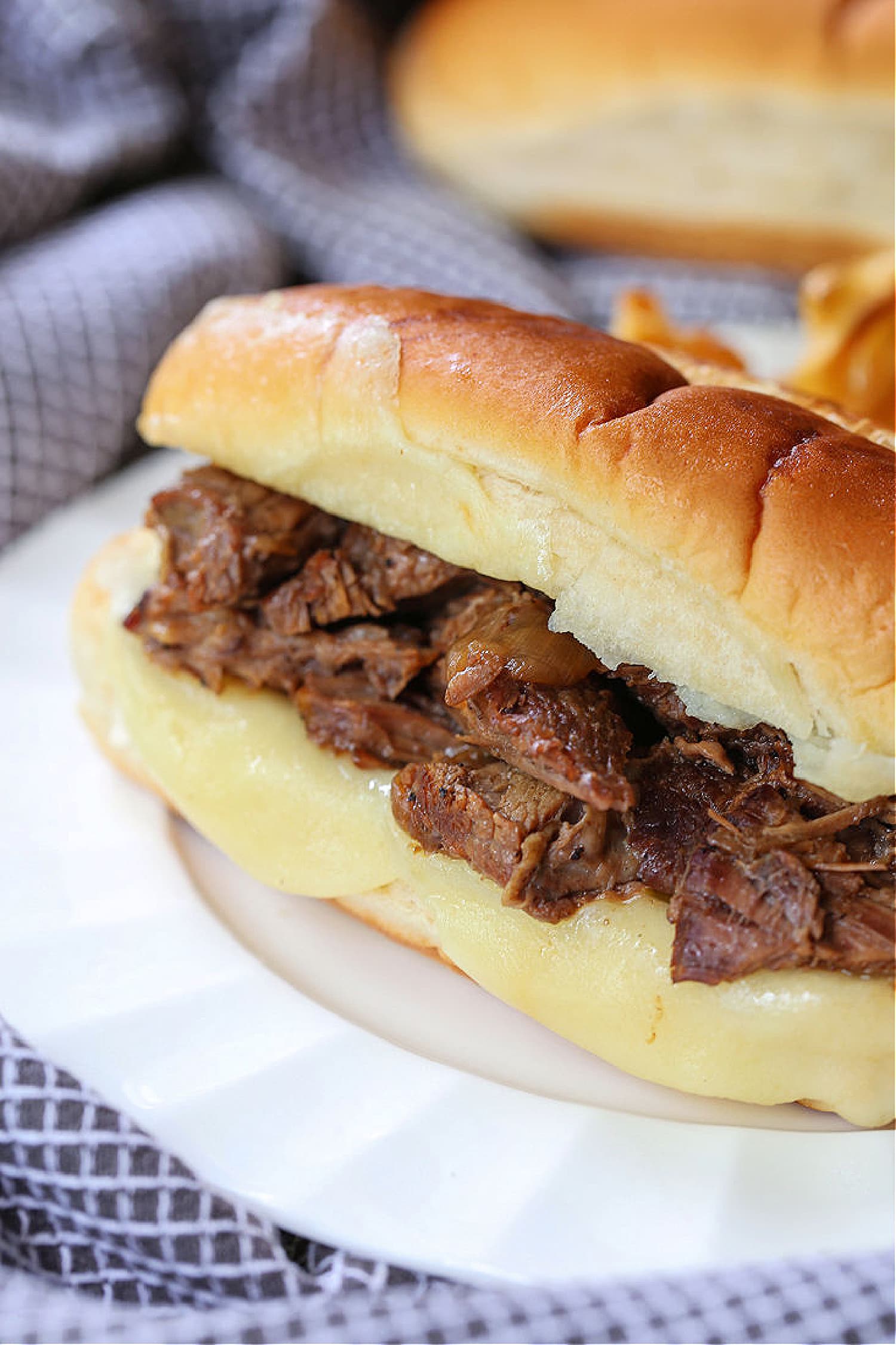 Make these Slow Cooker French Dip Sandwiches for parties or easy dinner nights! Tender, shredded beef with an au jus gravy for dipping! french dip sandwich in plate